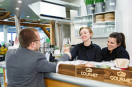 Zwei Mitarbeiterinnen hinter eine Theke von Gourmet Event die einem Gast ein Glas Wein überreichen